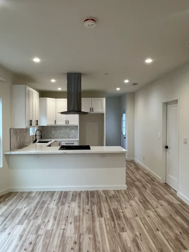 An empty kitchen with wood floors and white cabinets.