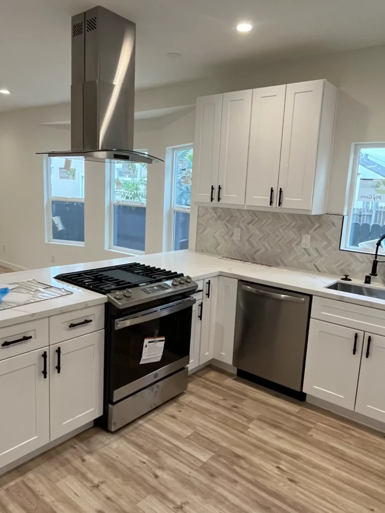 A white kitchen with stainless steel appliances and hardwood floors.