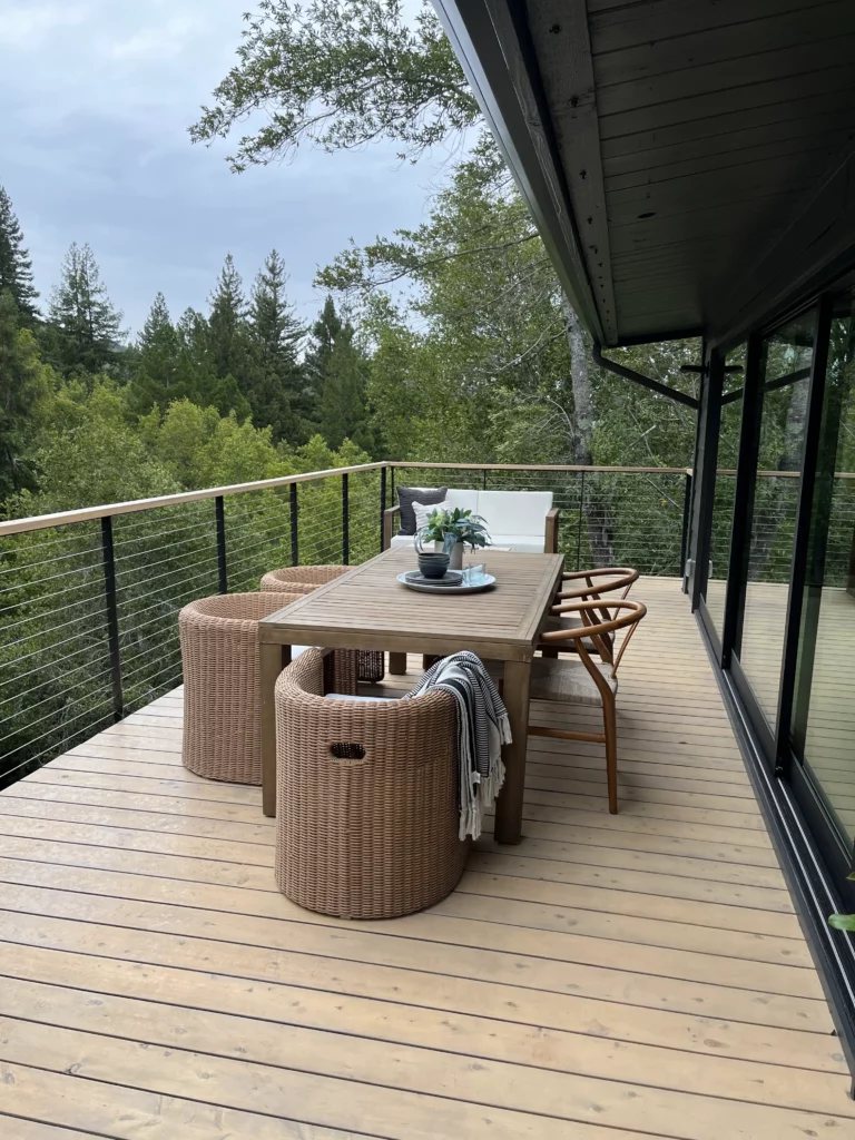 A deck with a table and chairs overlooking a wooded area.