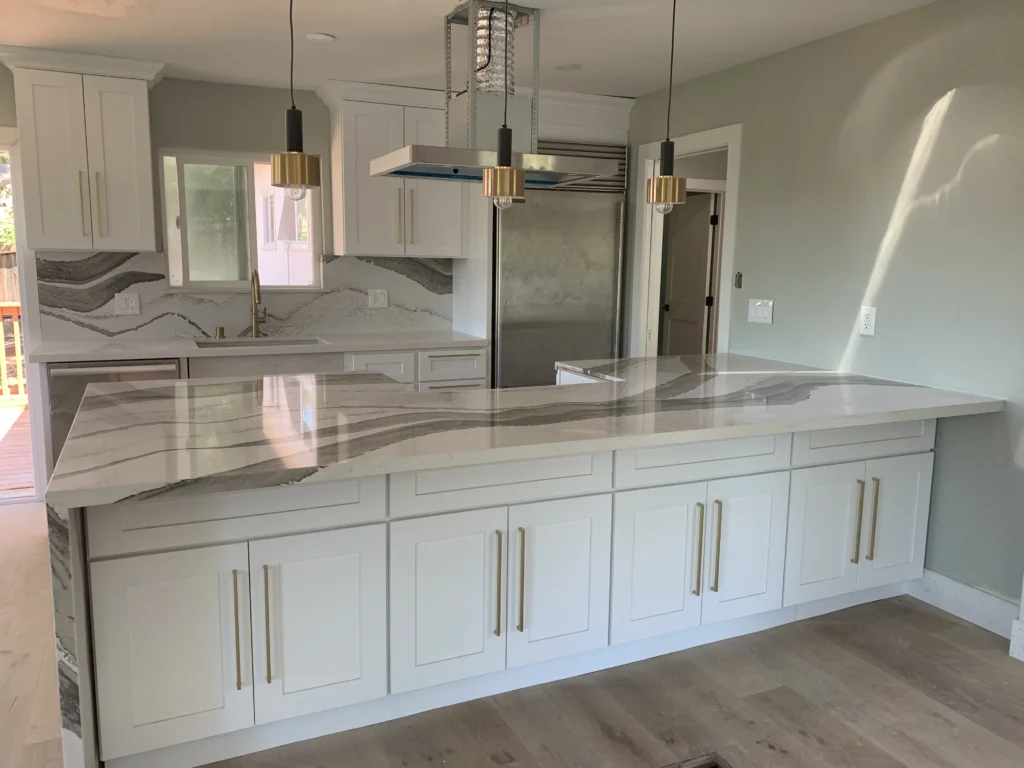 A kitchen with white cabinets and marble counter tops.